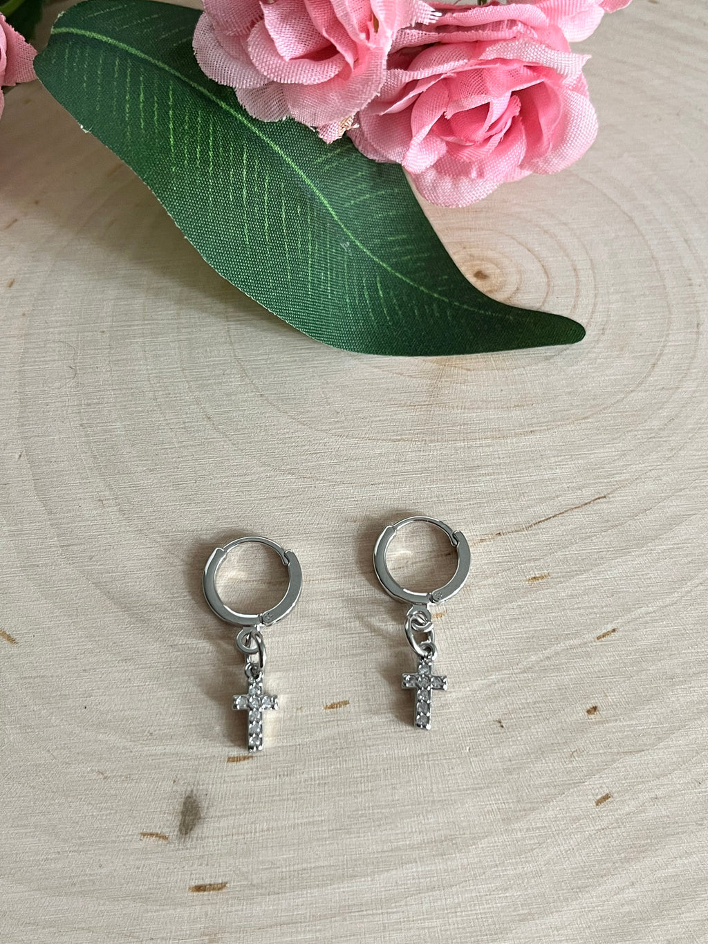 Silver huggie hoop earrings with dangling cross charms on a light wood background