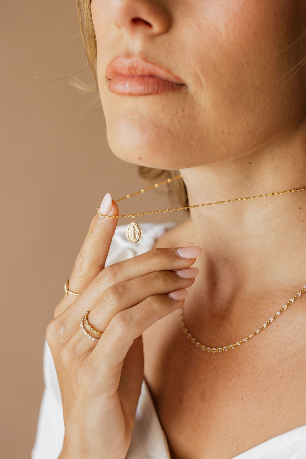 Gold chain necklace with oval medal pendant, hands holding the chain