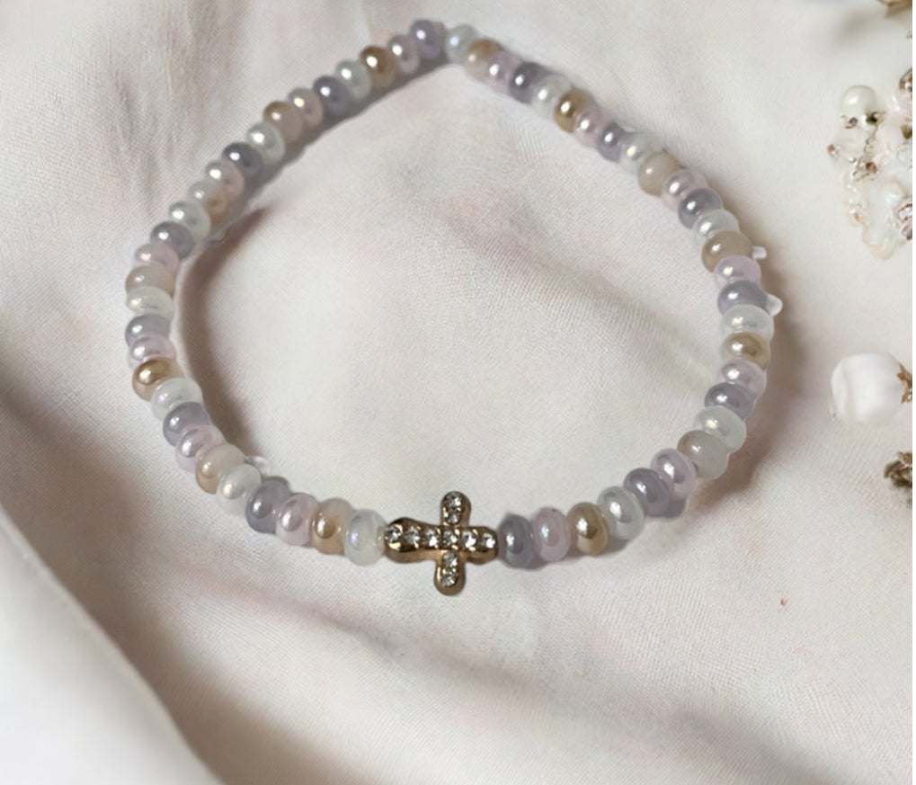 Bead bracelet with pale pink and white beads and a gold cross center charm