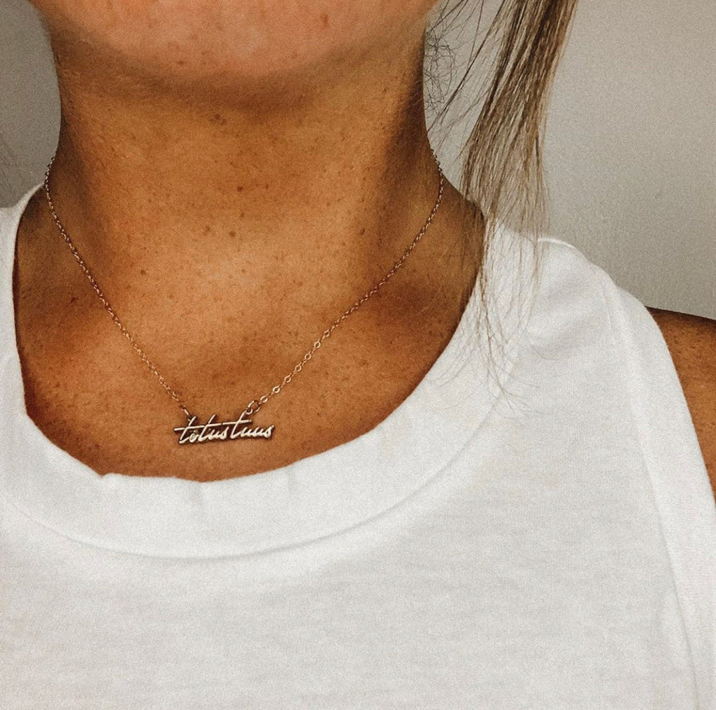 Gold-tone script pendant necklace worn at collar on white top