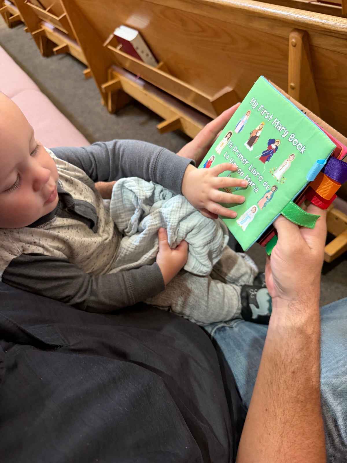 Baby lying on a couch holding a green fabric Mary colors book with ribbon ties.