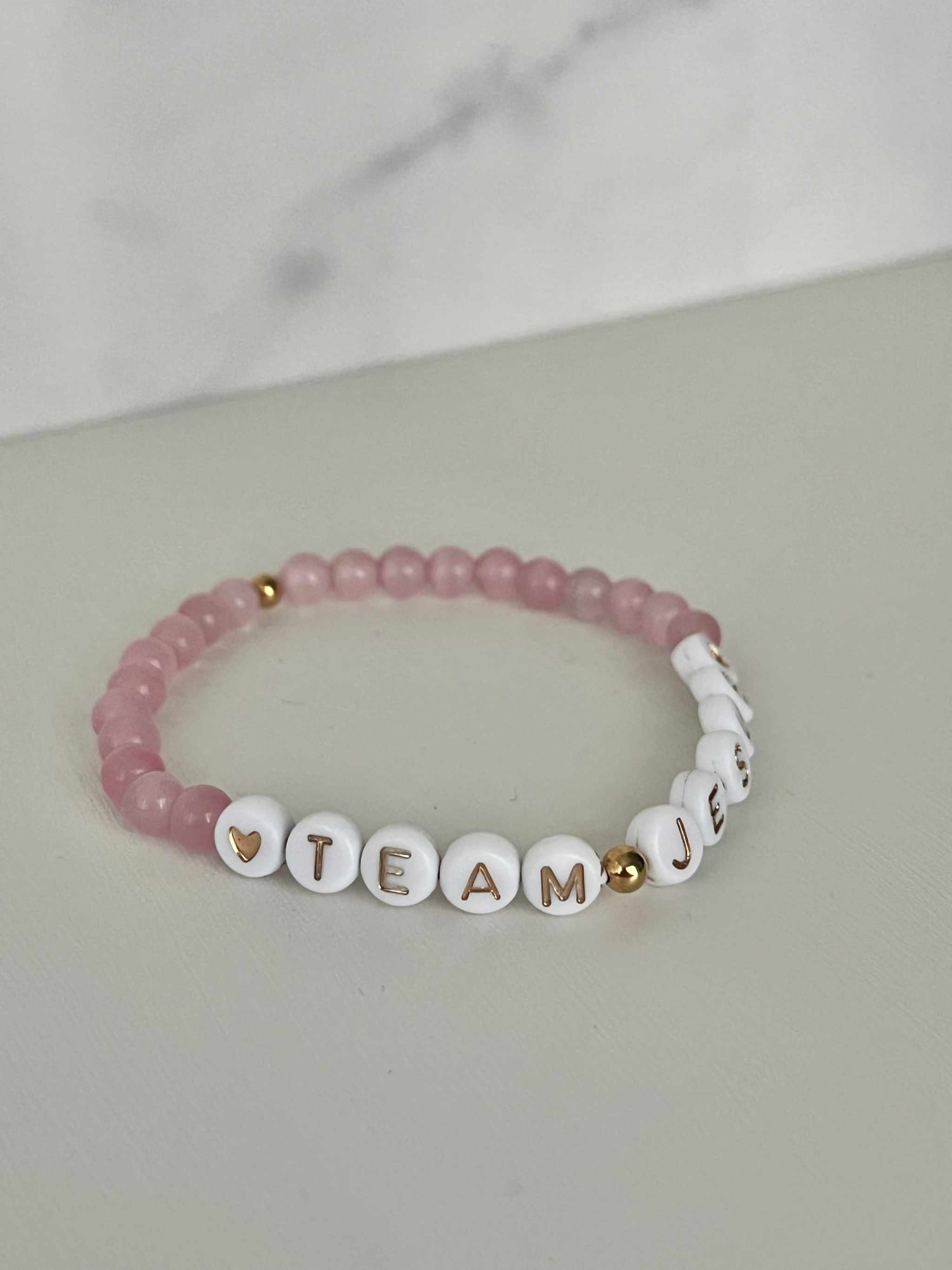 Opal-like iridescent beaded bracelet with pink beads and white letter charms spelling TEAM