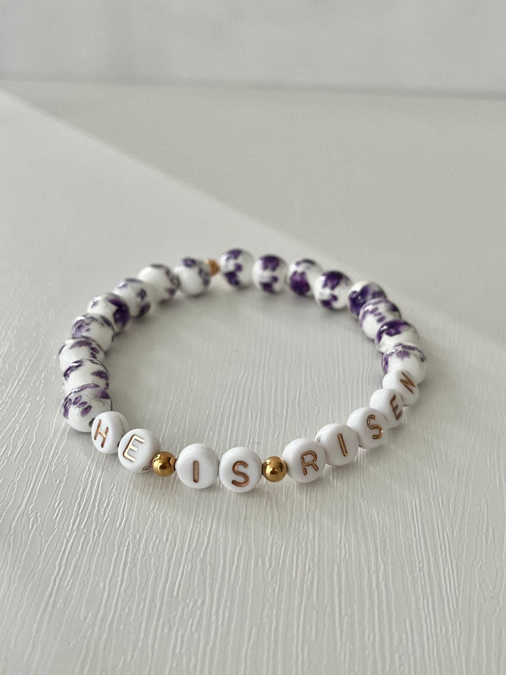 Bead bracelet with “HE IS RISEN” in white letters and purple patterned beads