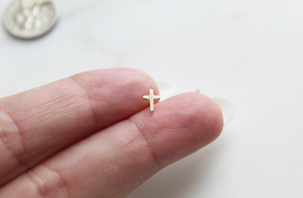 14k gold cross stud earring on fingertip, small cross shape