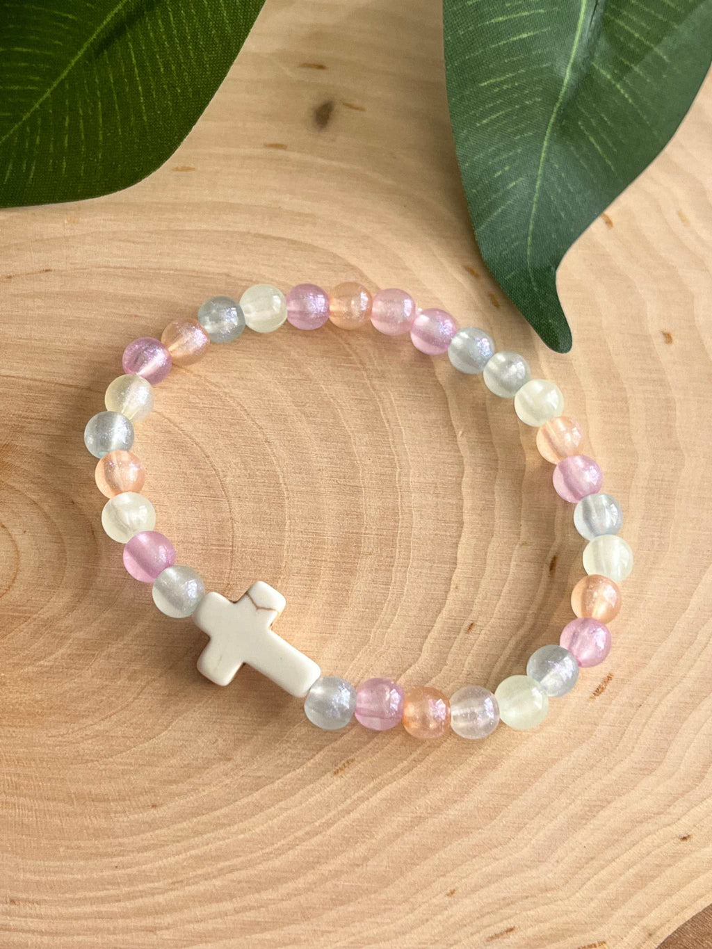 Pastel beaded bracelet with a white cross charm and multicolor beads around.