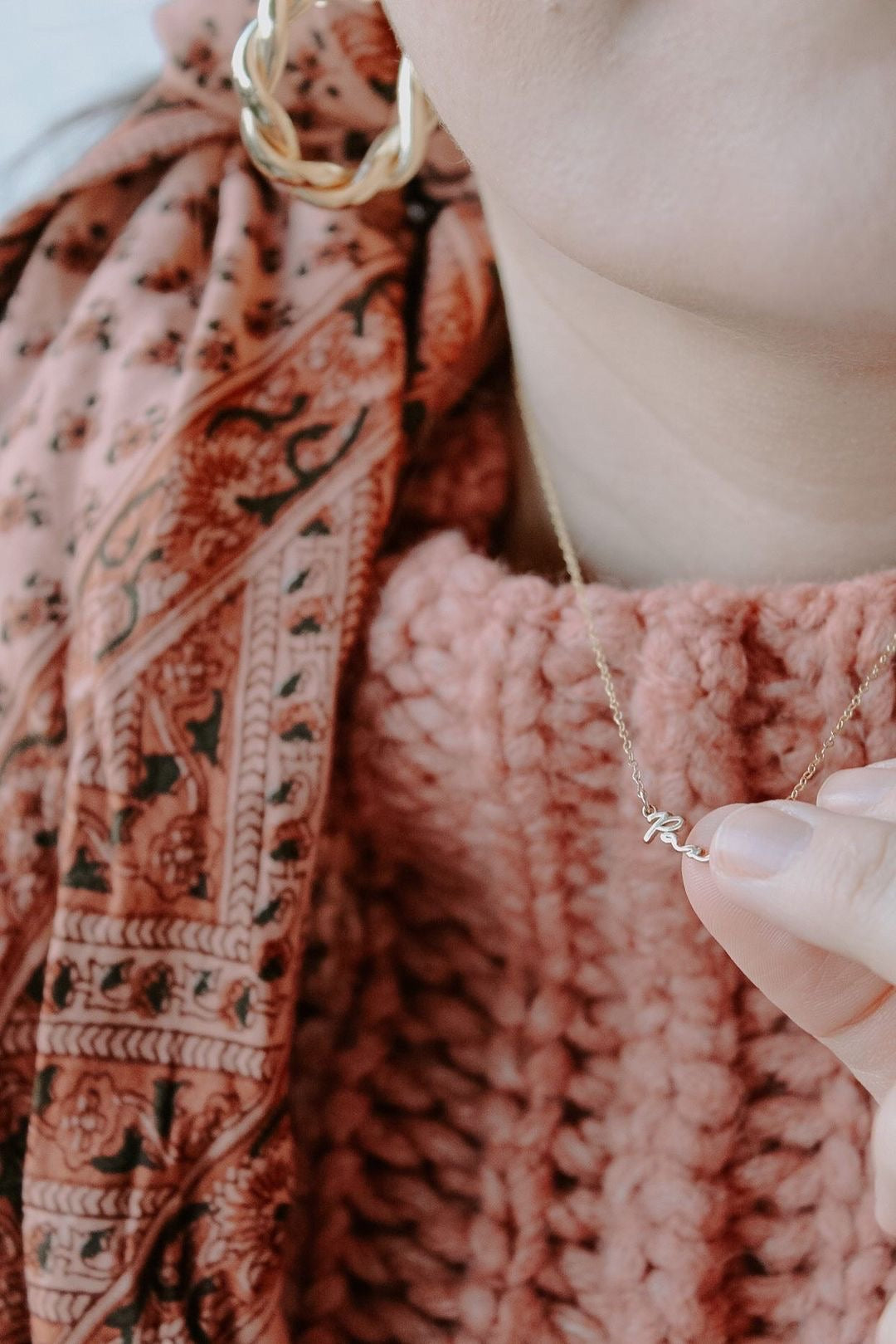 Gold Pax pendant necklace on pink knit sweater, held near the clasp