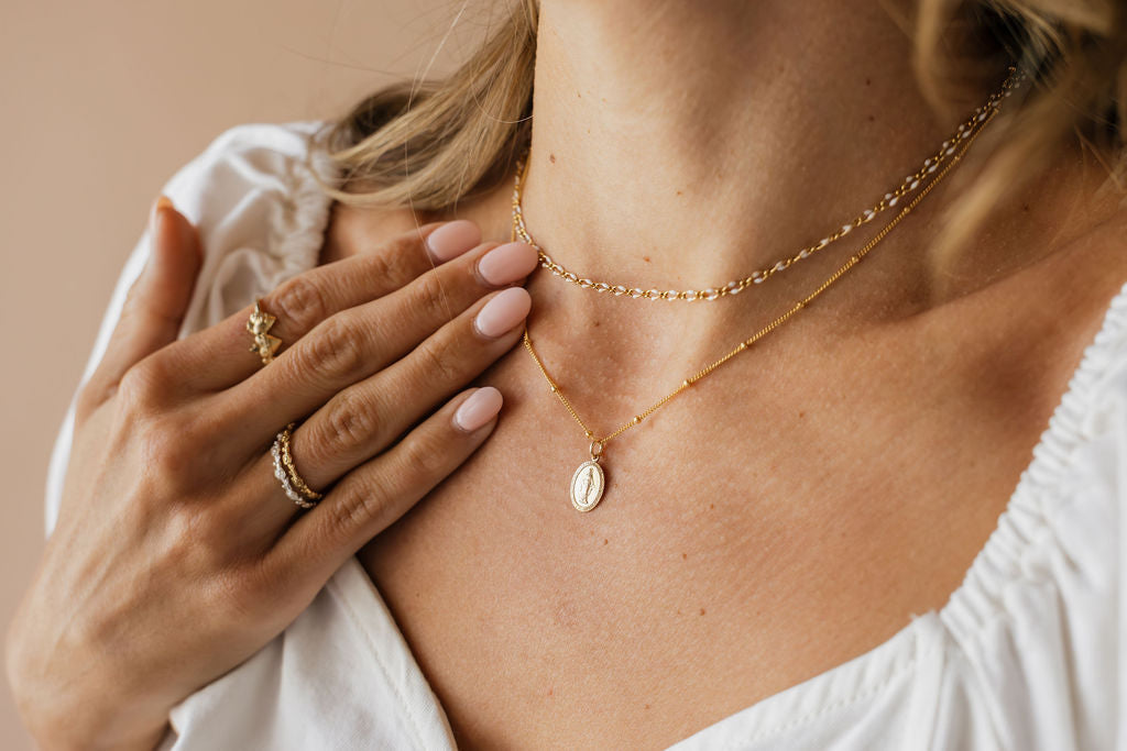 Gold flat-link necklace with oval medal pendant shown on collarbone