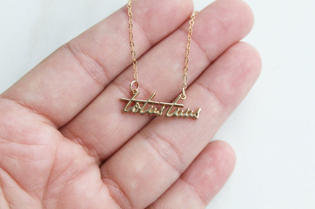 Gold-tone Totus Tuus pendant necklace in an open palm