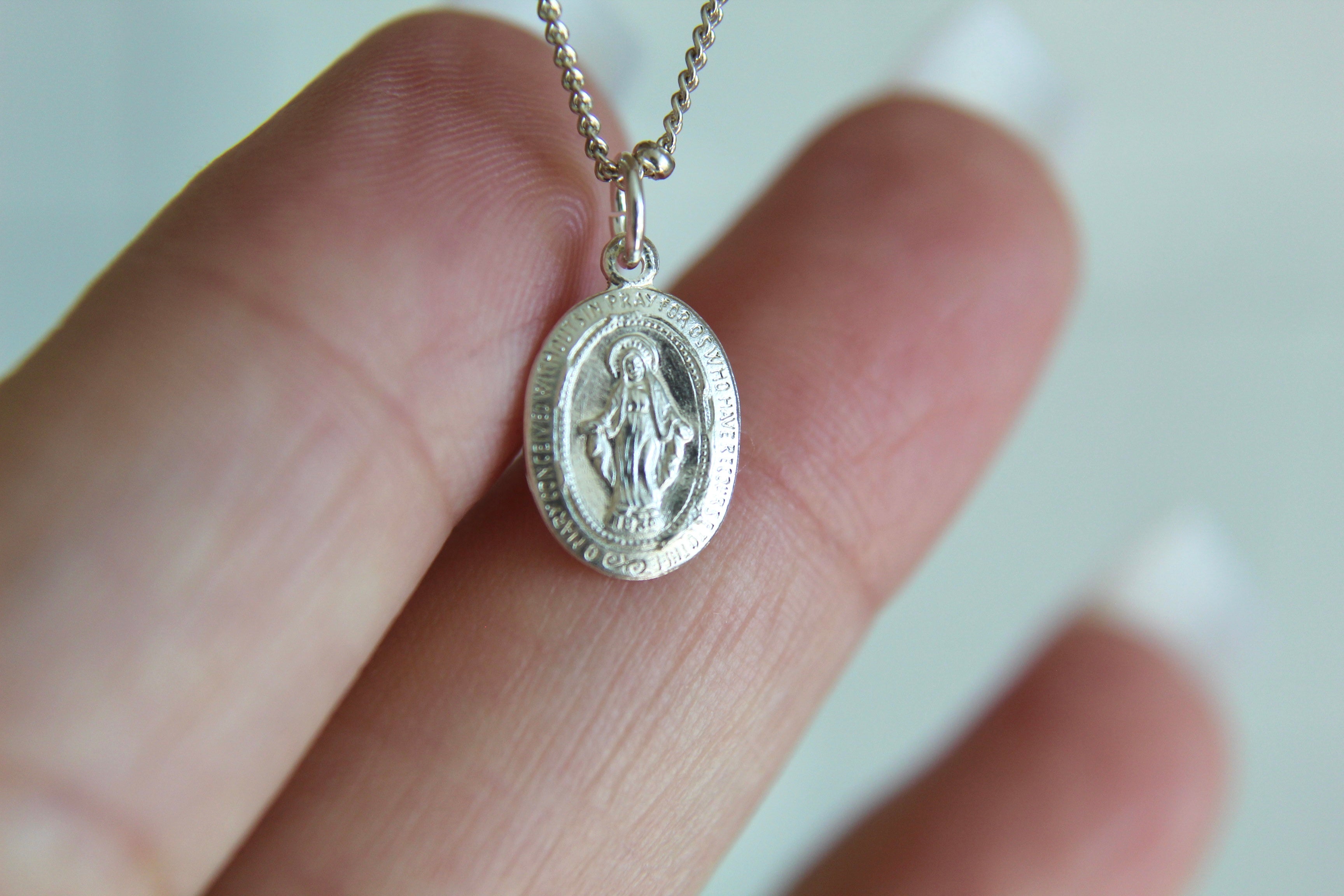 Silver miraculous medal pendant necklace with oval medal and chain in hand