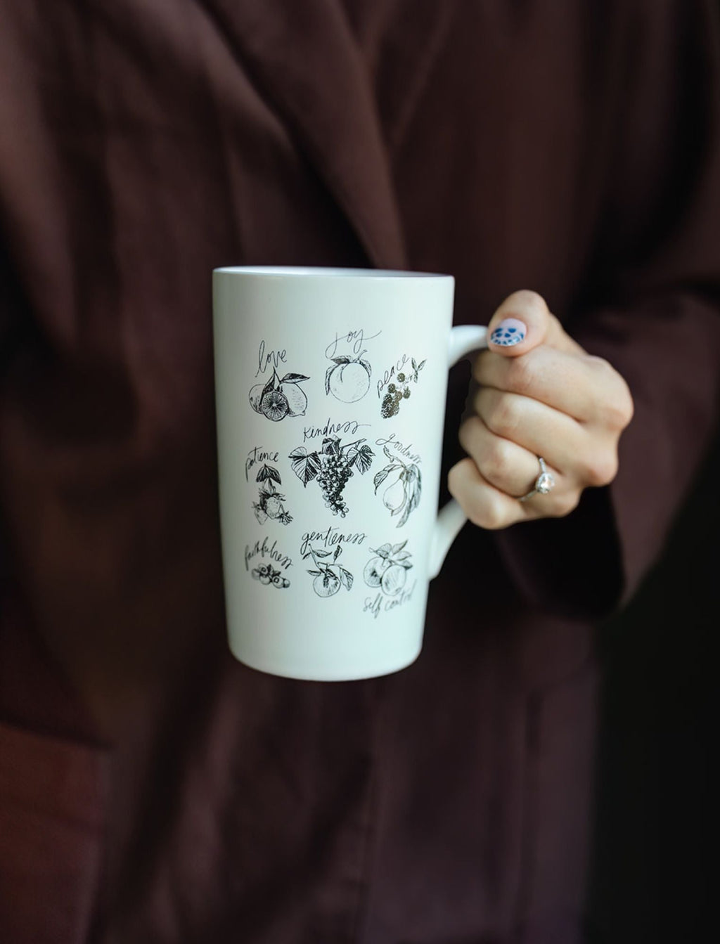 White ceramic mug with black fruit-and-leaf line art, held in a hand