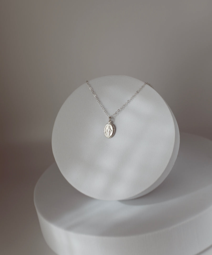 Silver medal pendant necklace on delicate chain, displayed on round white pedestal