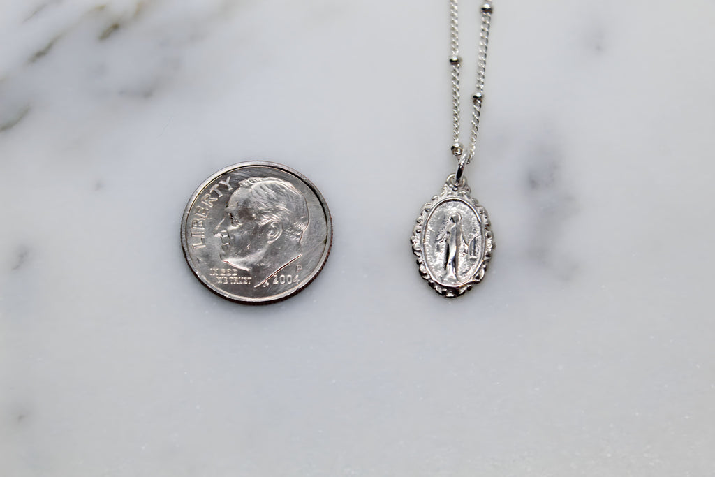 Silver-tone oval medal pendant necklace shown next to a coin for scale