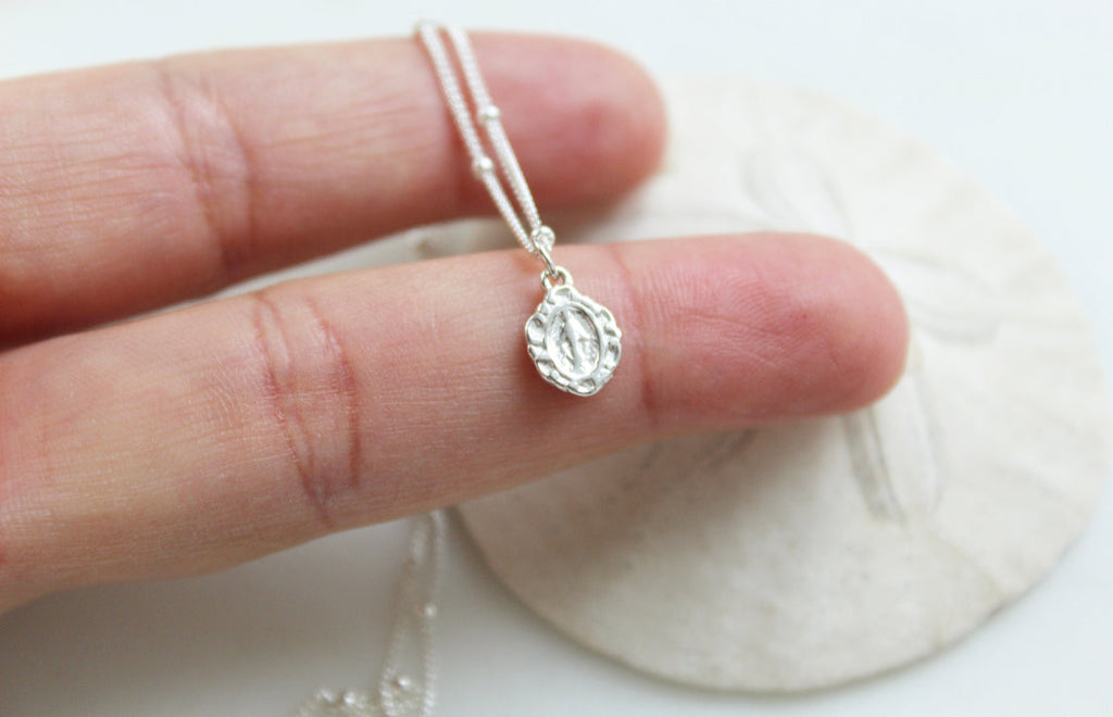 Sterling silver tiny medal pendant with textured bail and link chain, held in hand