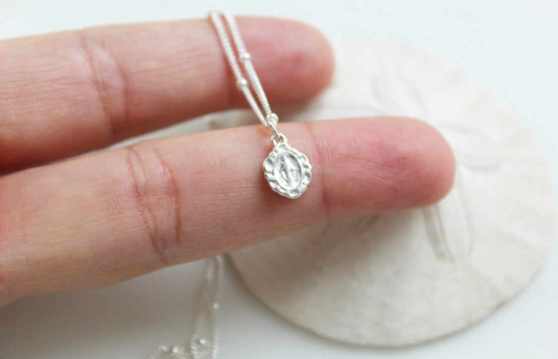 Sterling silver tiny medal pendant with textured bail and link chain, held in hand