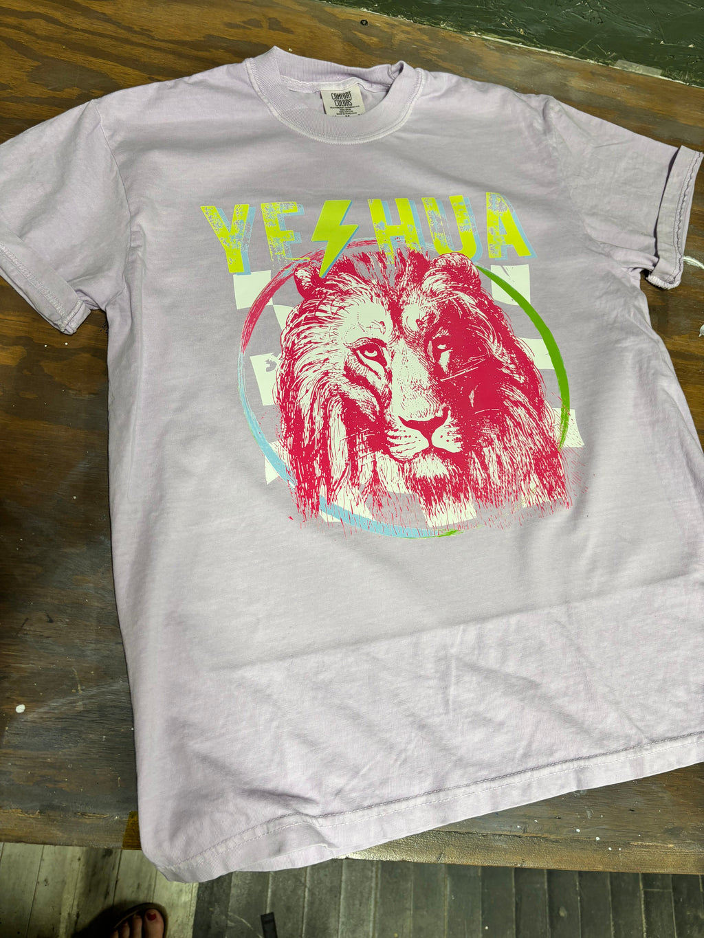 White t-shirt with green lettering and red lion head logo in multicolor circle