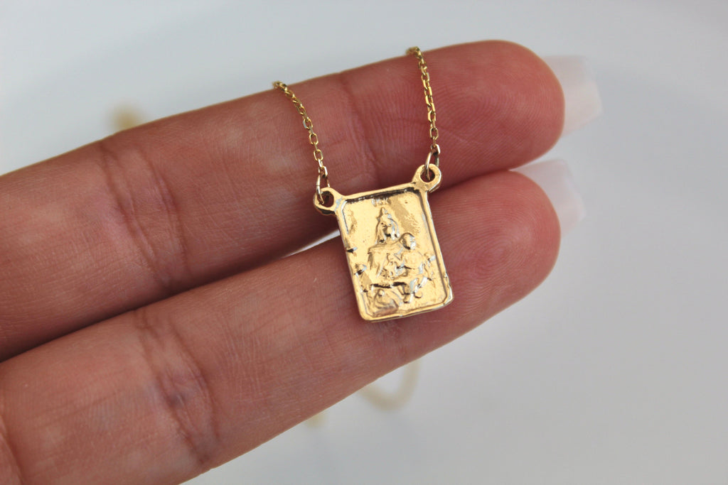 Square 14K gold scapular pendant with figure relief shown in hand on chain