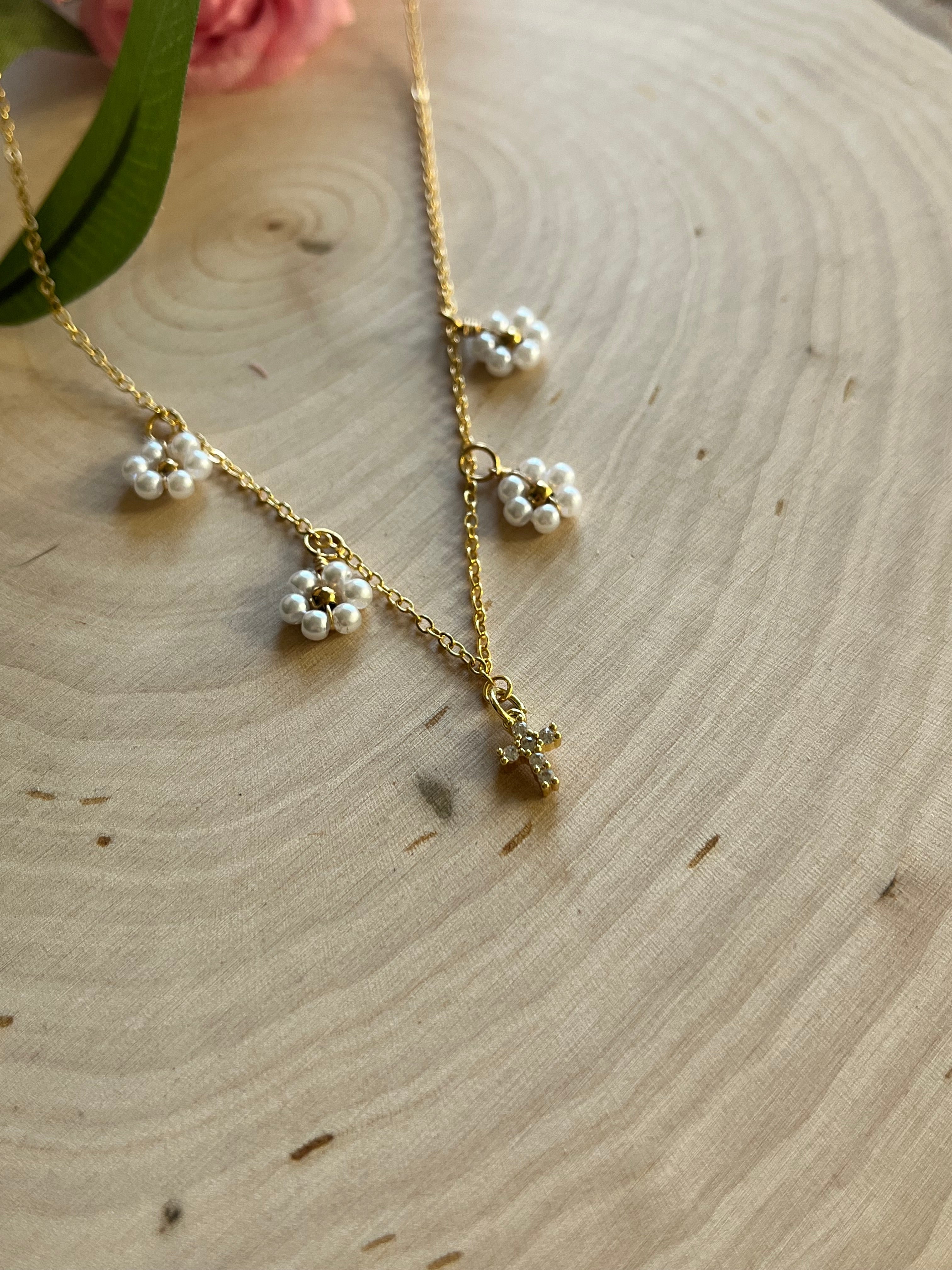 Gold cross pendant necklace with white daisy charms in an angled close-up