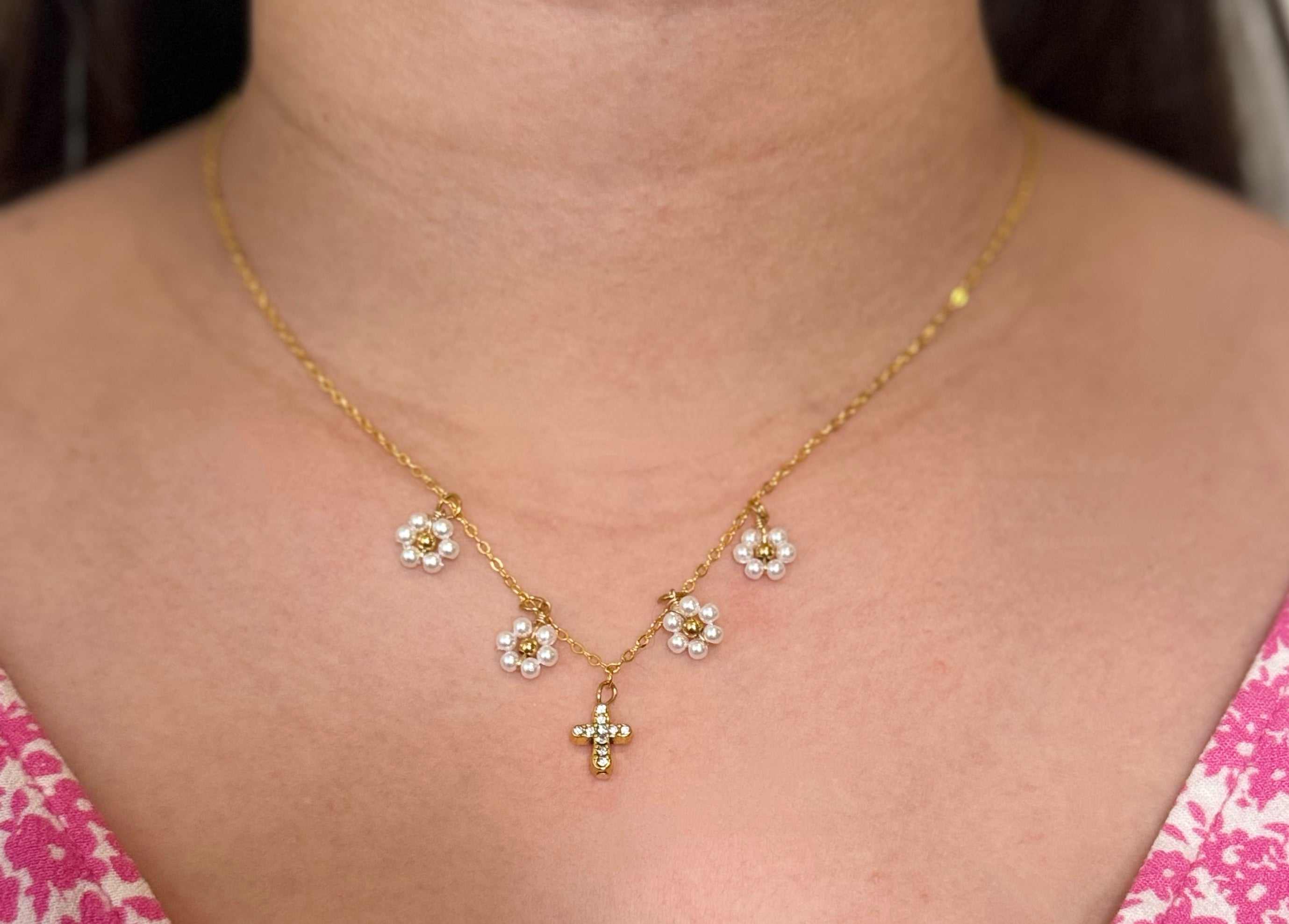 Gold cross pendant necklace with white daisy charms, worn on the neck