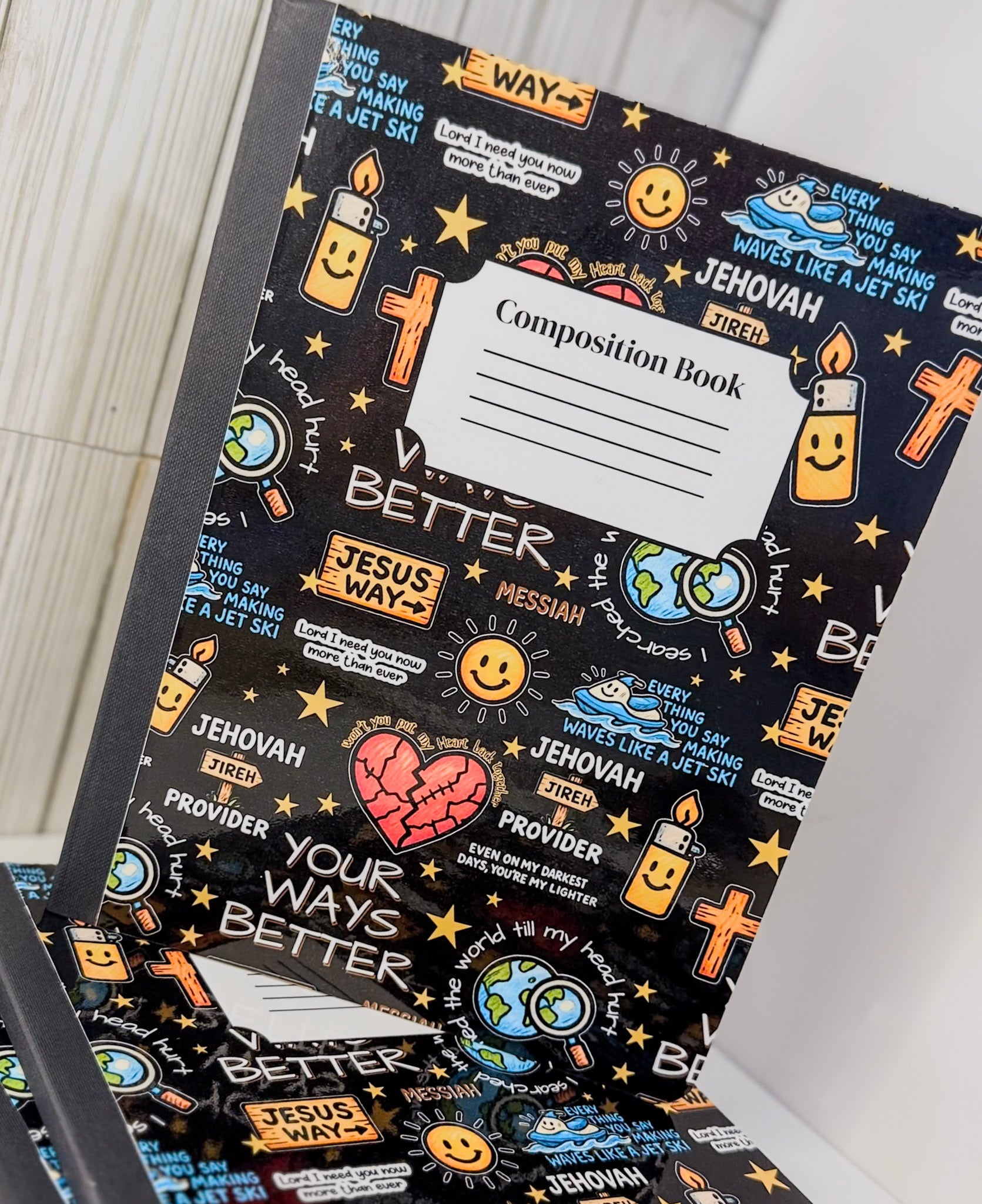 Black composition book with 'Composition Book' label and colorful Christian icons on cover