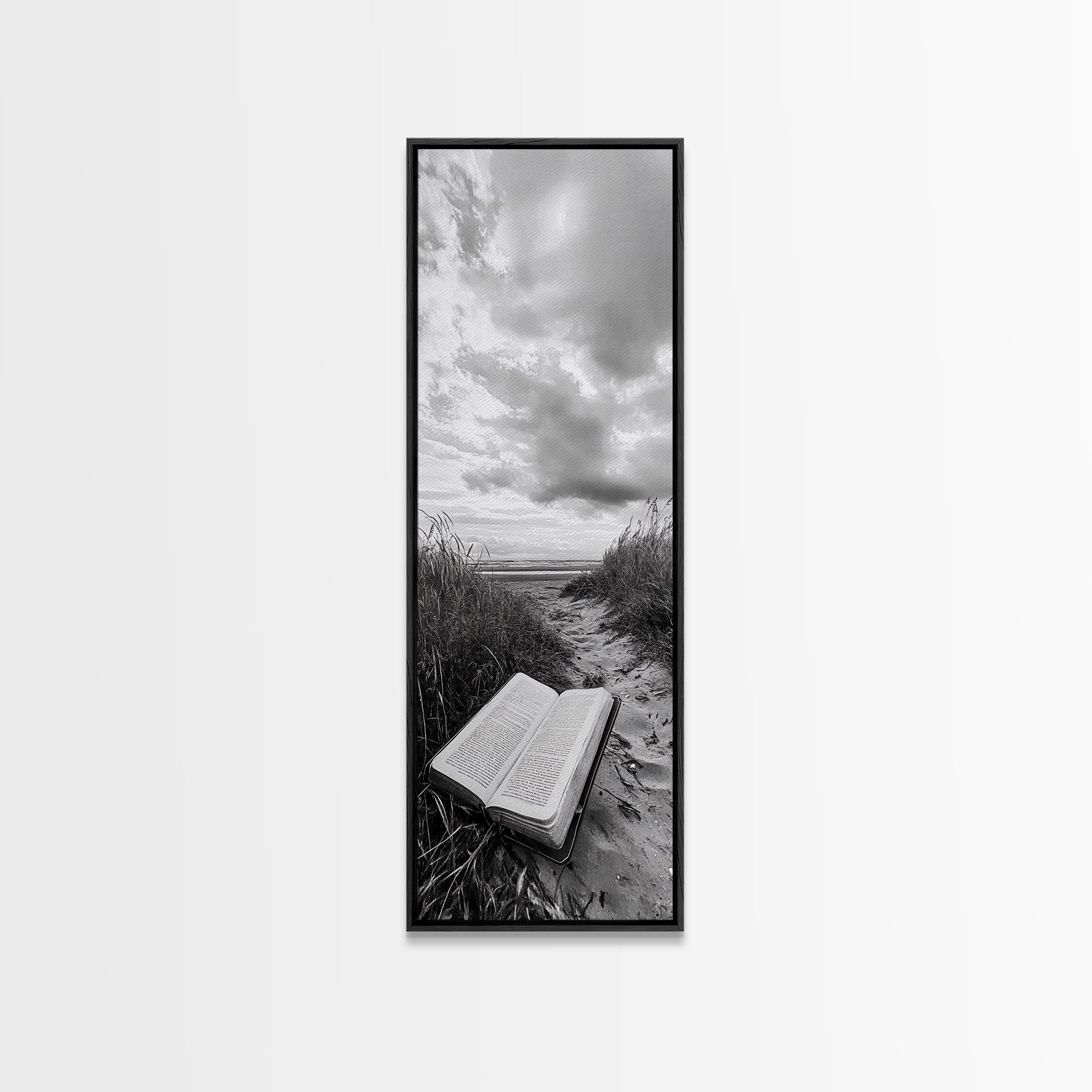 Black framed canvas print of open Bible on a sandy beach path under cloudy sky