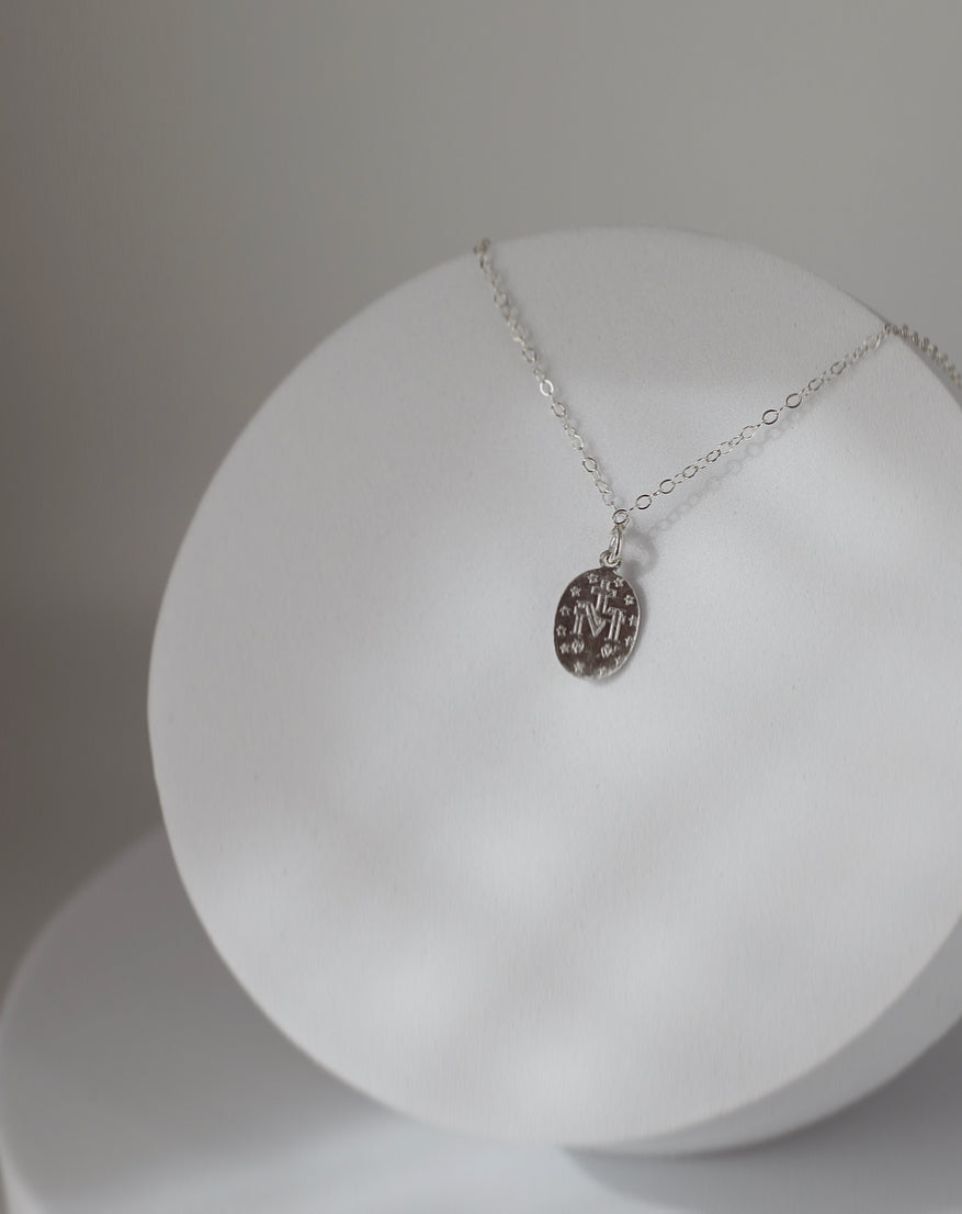 Silver oval medal pendant necklace with delicate chain, displayed on round stand