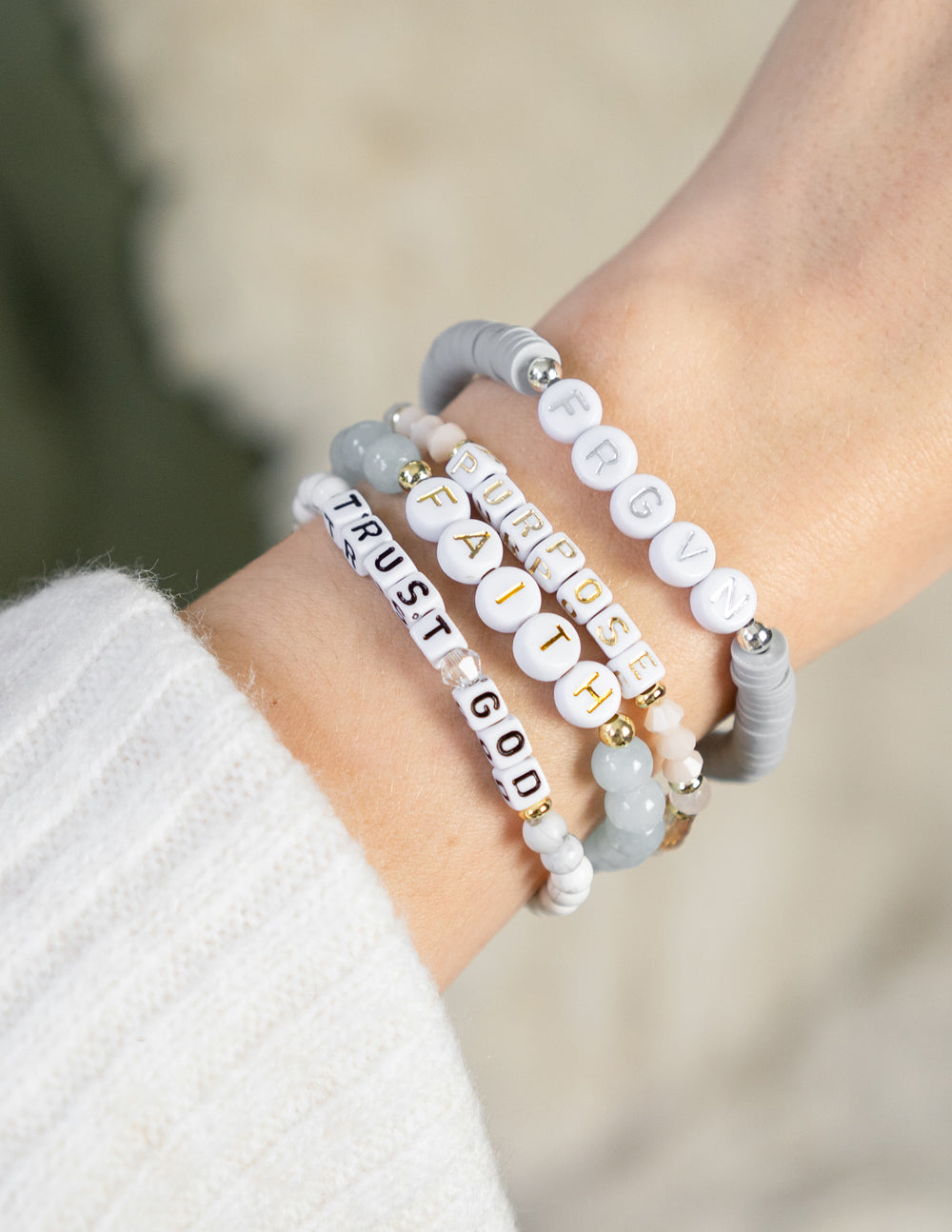 Beaded "TRUST GOD" letter bracelet on wrist with white, gray, and gold accents