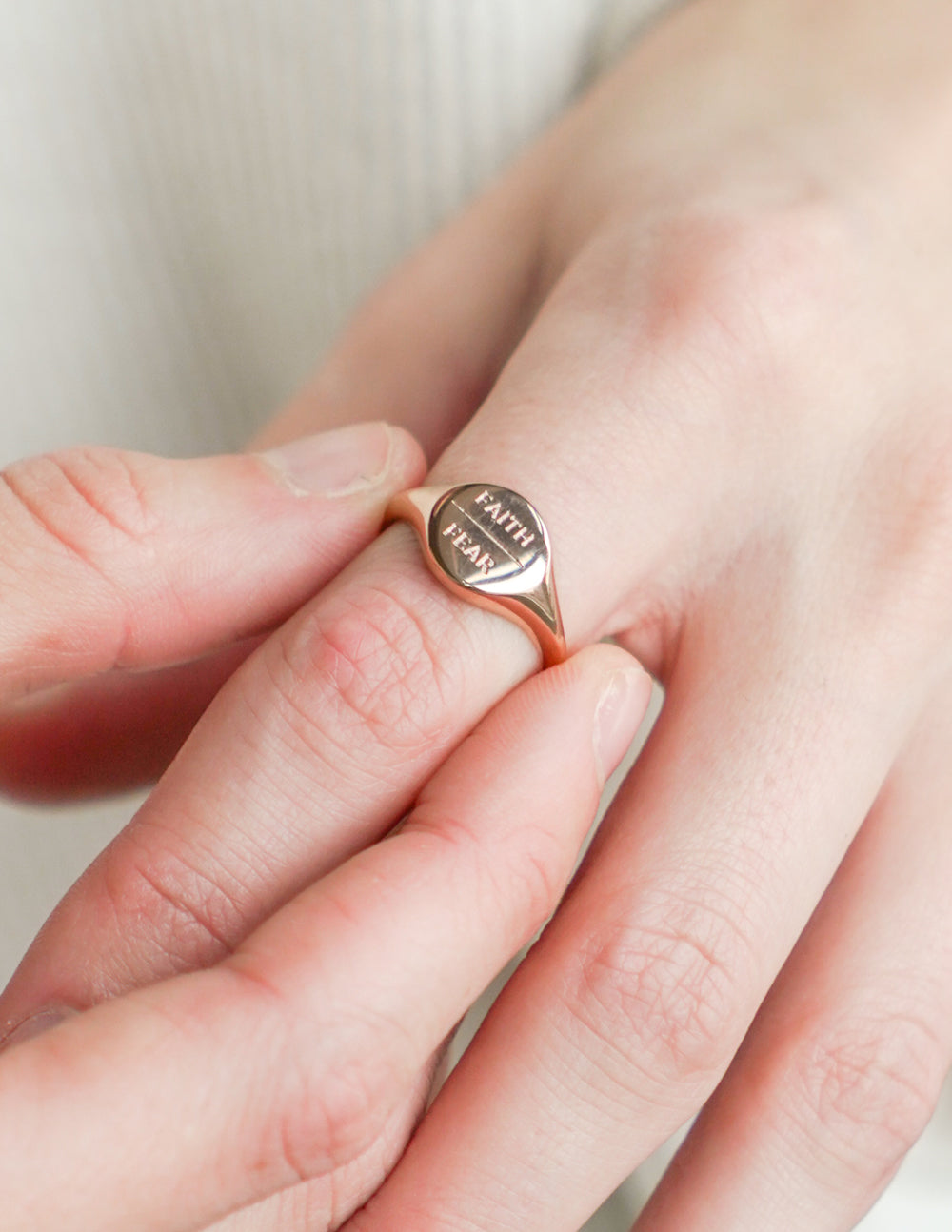Rose gold signet ring worn on finger, 'FAITH' and 'FEAR' engraved