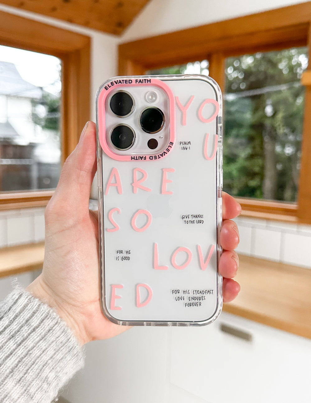 Clear phone case with pink lettering and four camera cutouts, held in a hand