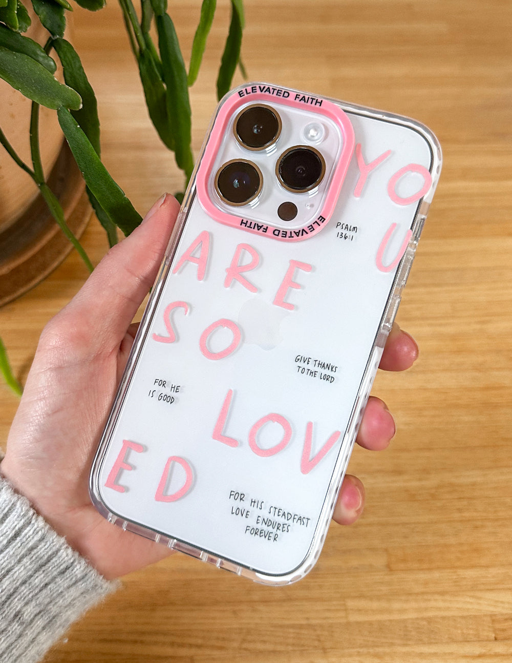 Clear phone case with pink lettering and four camera cutouts, held over a tabletop