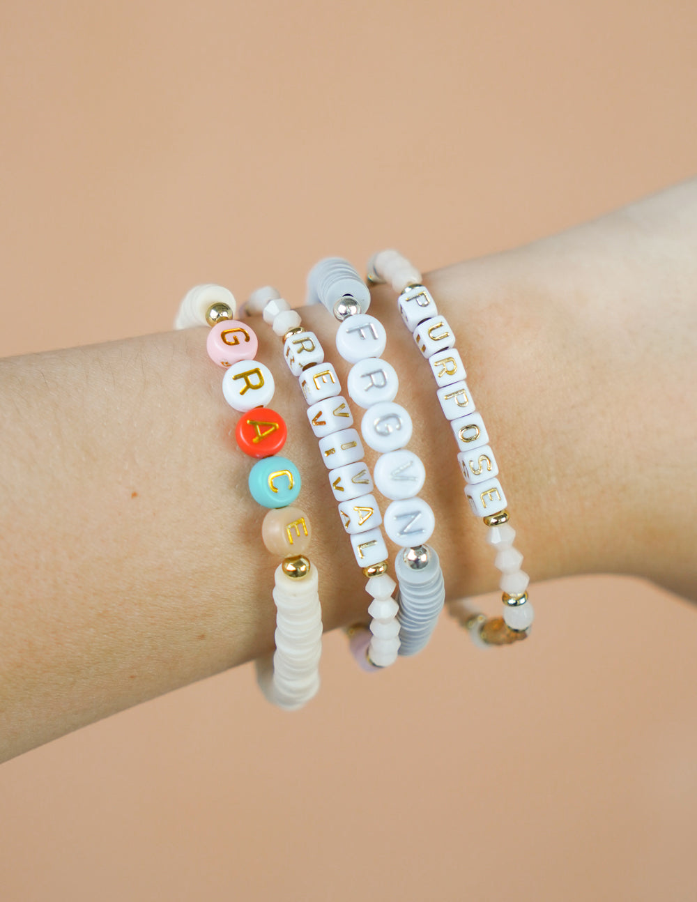 Stack of letter bead bracelets on wrist with colorful alphabet beads and gold charms