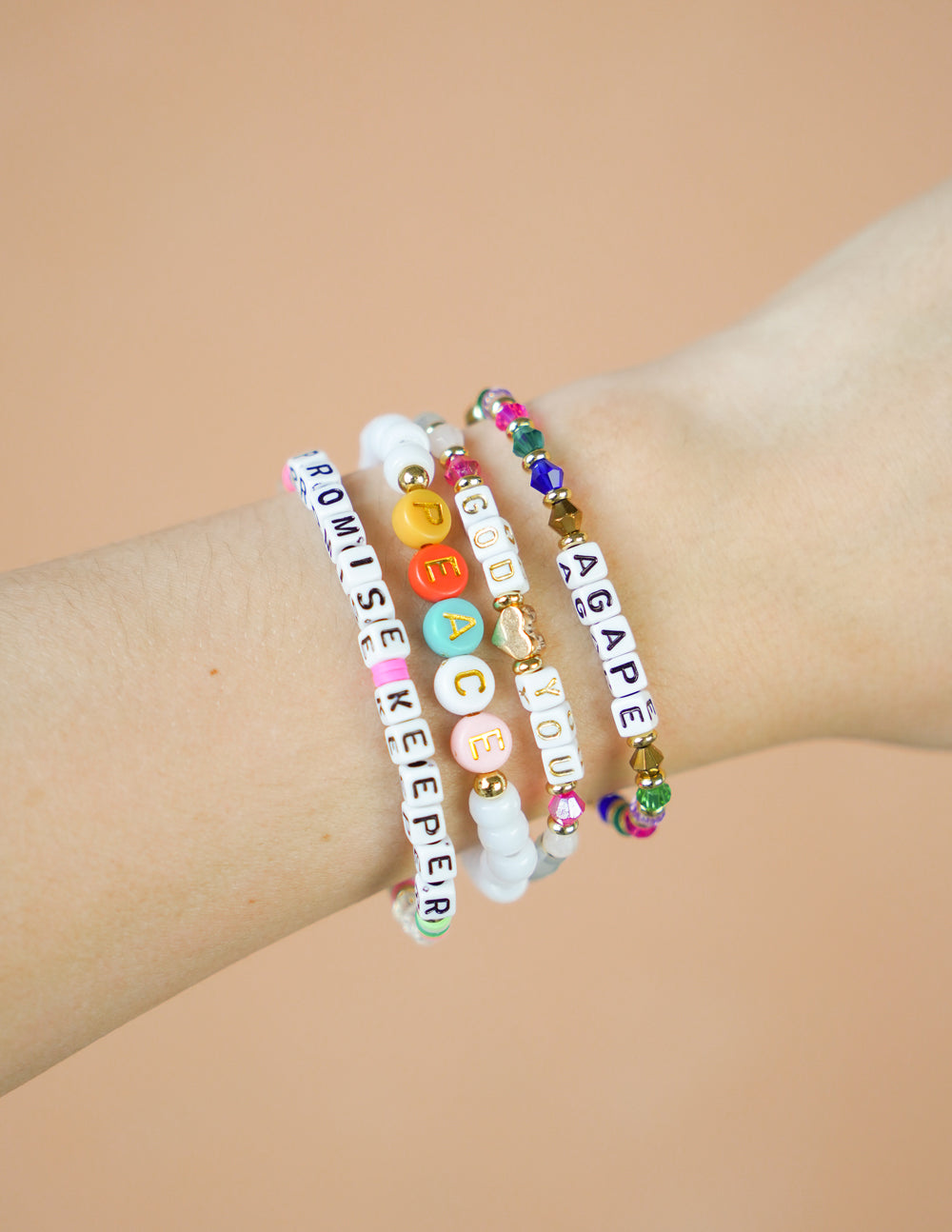 Stacked letter bracelets on wrist, white beads with colored letter and bead charms