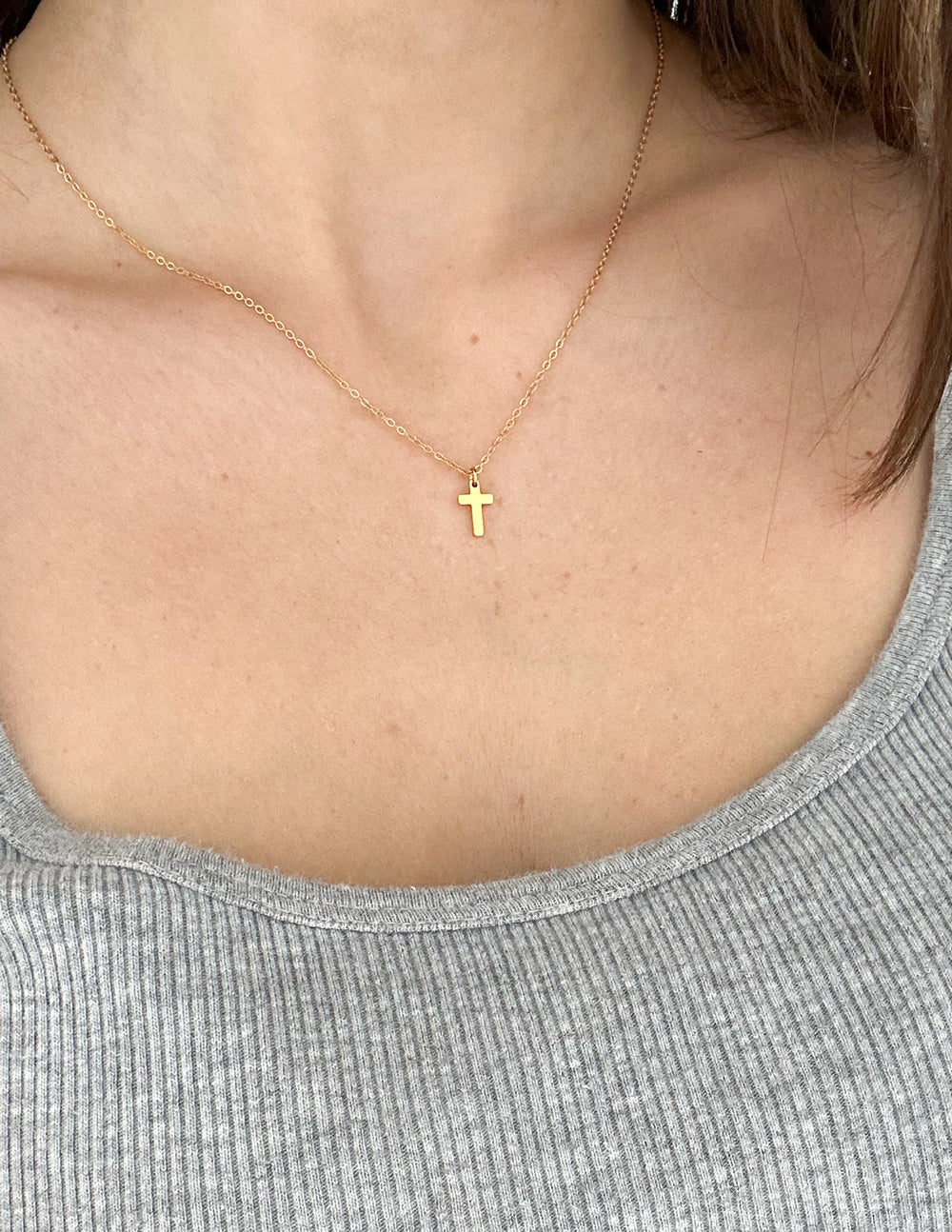 Gold cross necklace with small cross pendant at neckline on thin chain