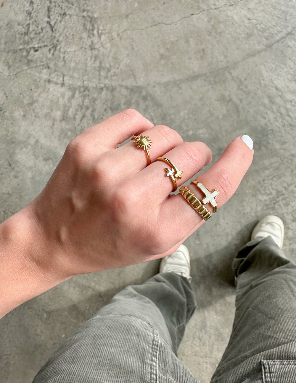 Gold cross enamel ring on finger with stacked gold bands