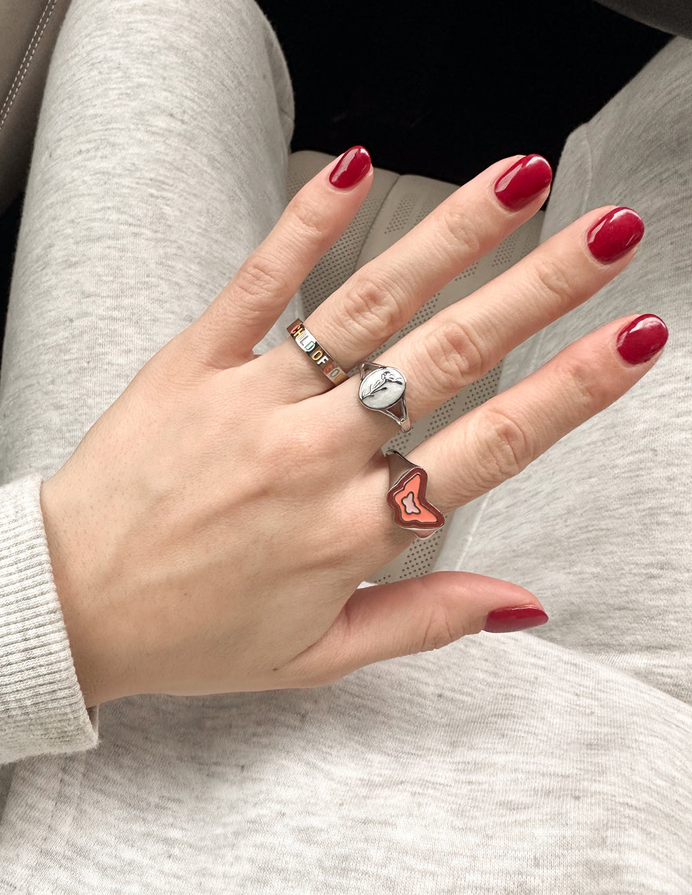 Pink enamel butterfly ring on hand, silver band visible with red nails