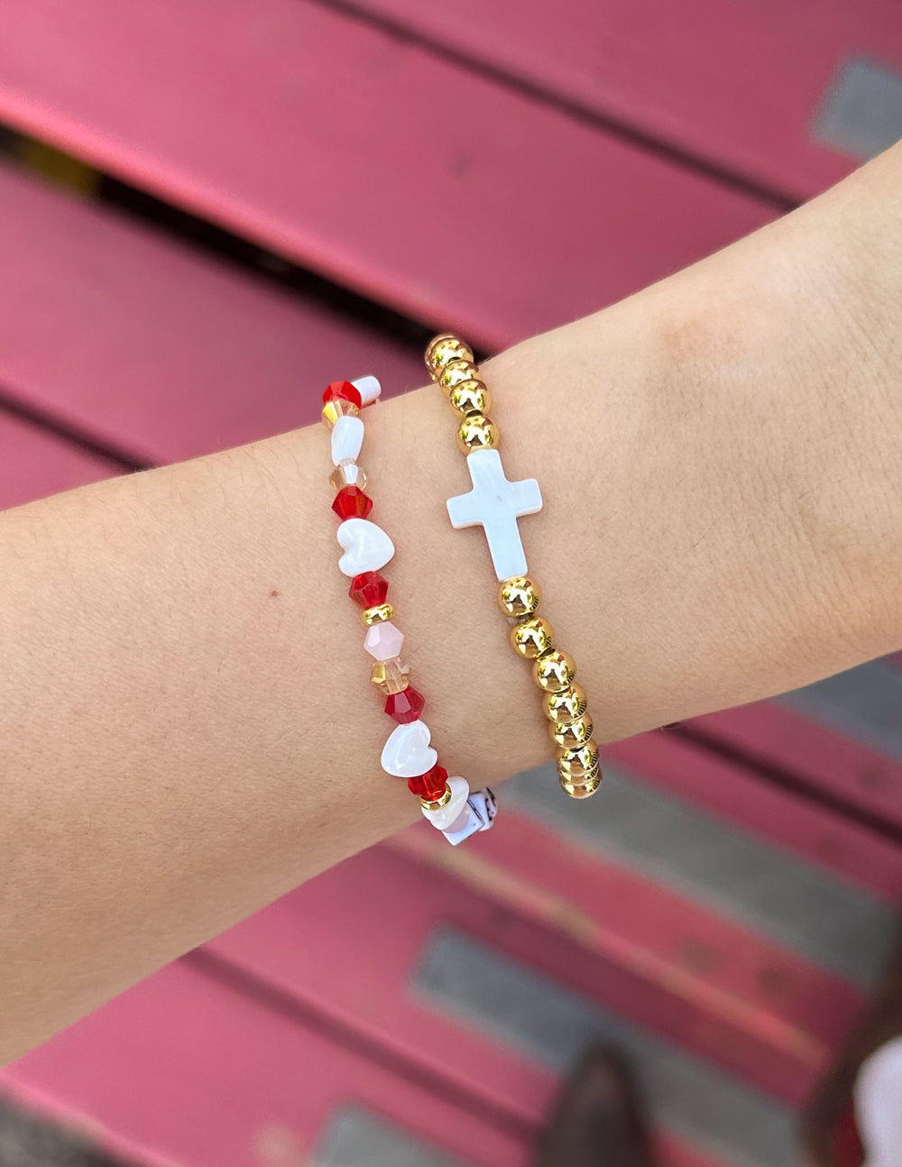 Gold beaded cross bracelet with a white cross charm on wrist