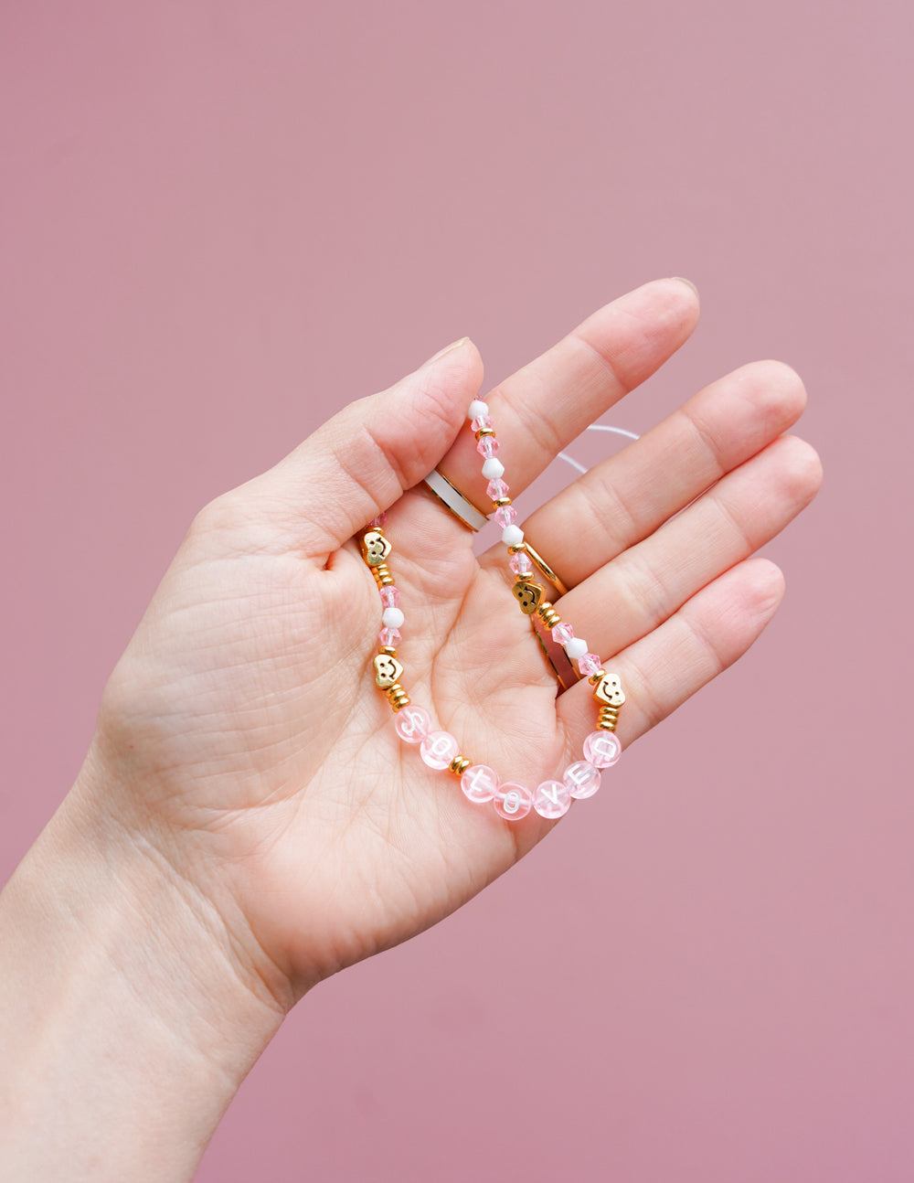 Pink and gold beaded phone charm held in hand with round gold connector beads