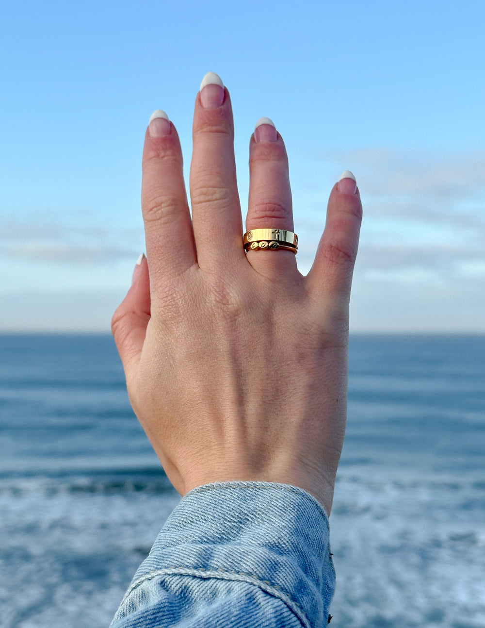 Gold band ring with cross emblem and small clear stones along the top edge