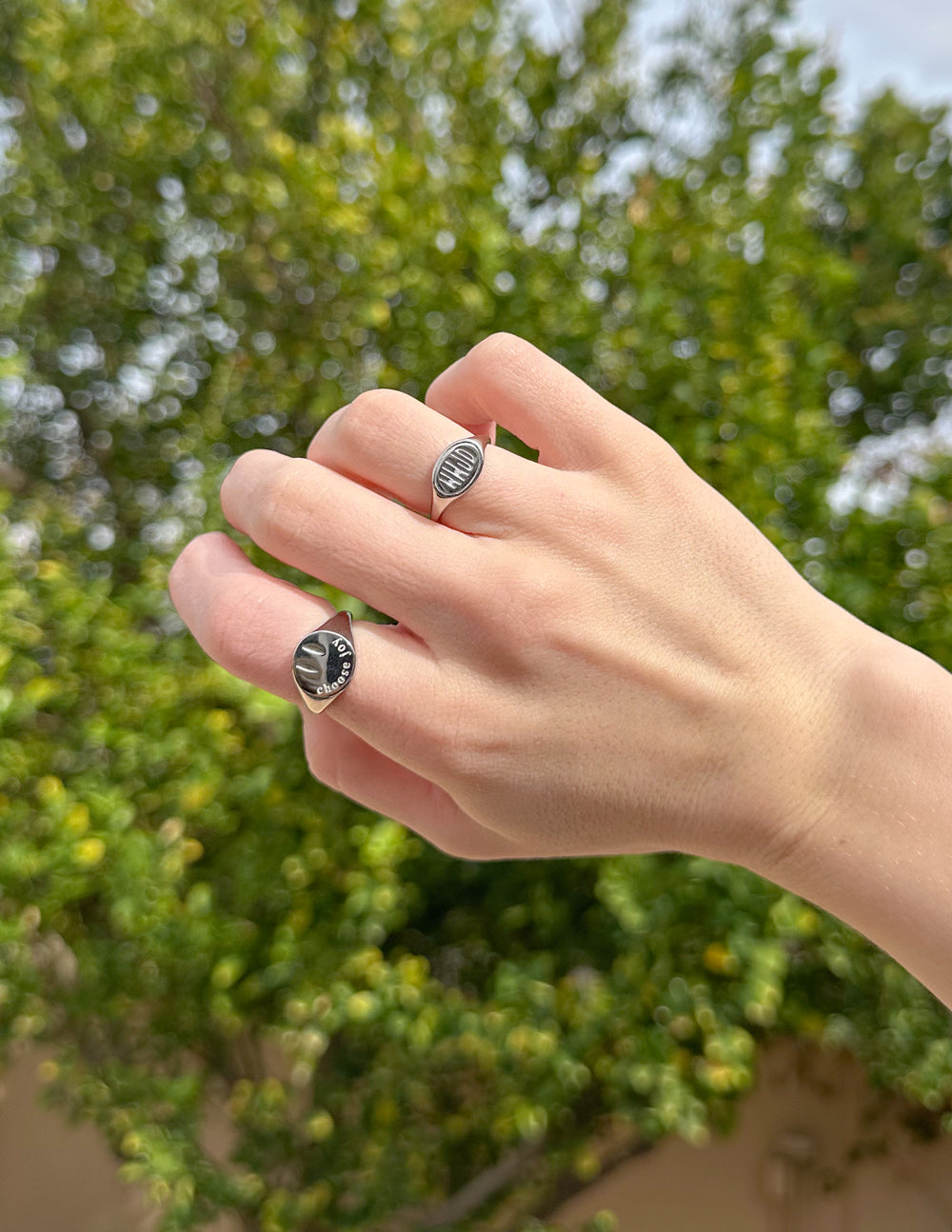 Silver rings on hand; round faces with 'Choose Joy' and a striped pattern.