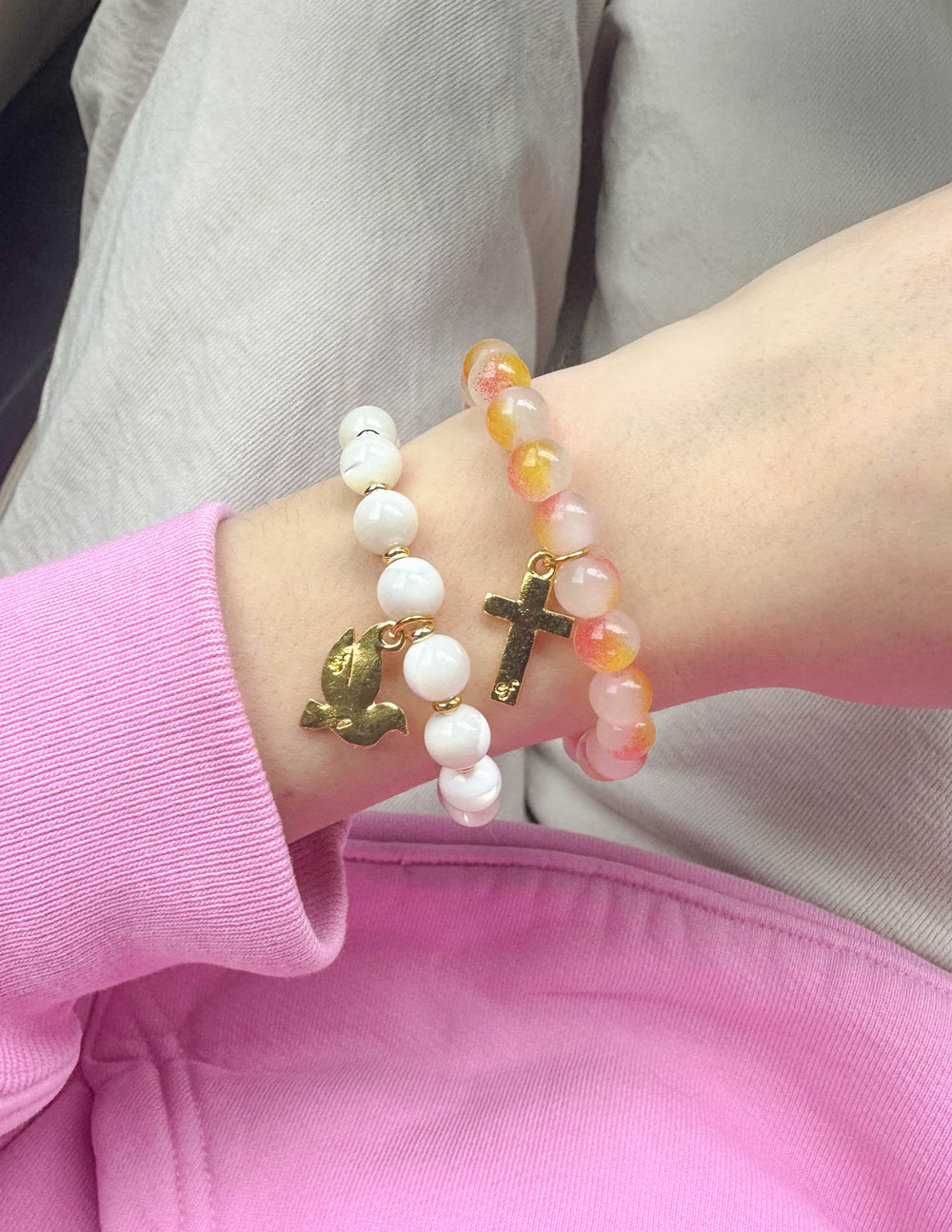 Stacked beaded bracelets with white and peach beads, featuring gold cross and dove charms
