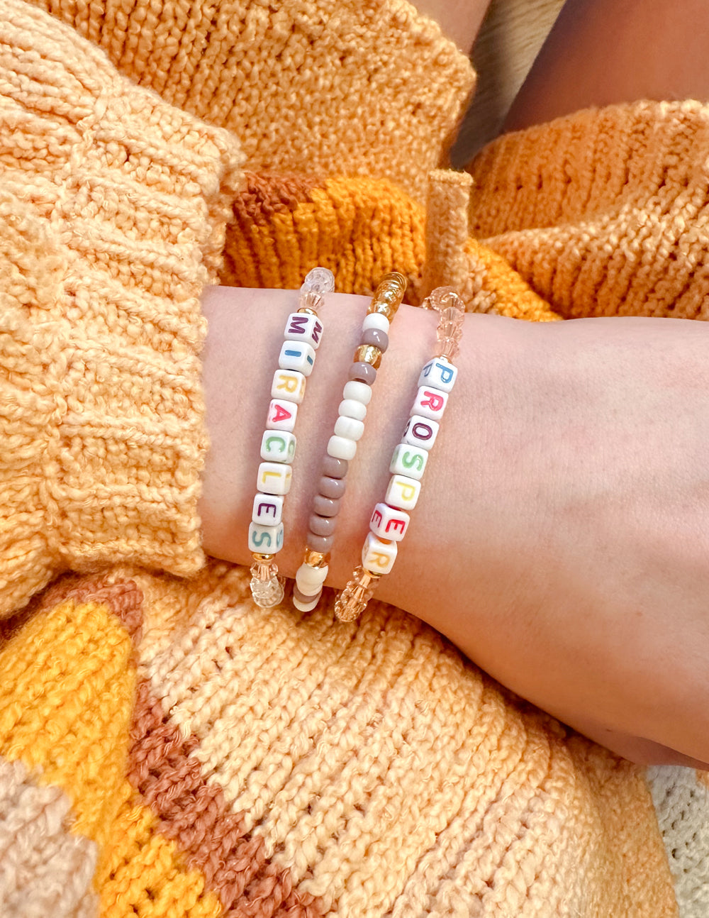 Stacked beaded bracelets with multicolor letter beads and small charm beads.