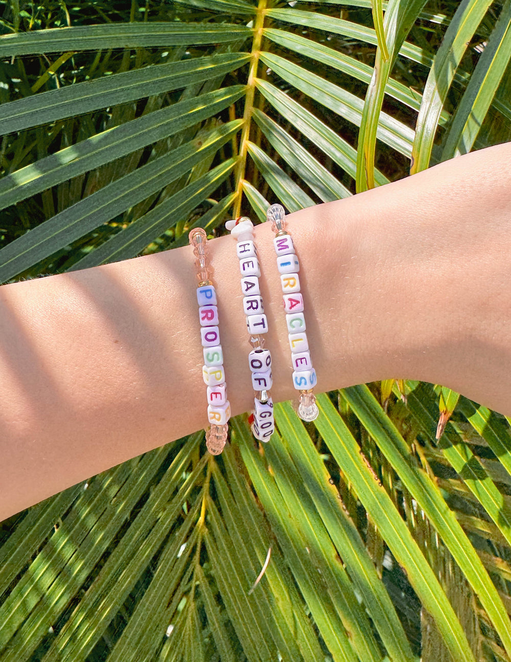 Stack of beaded letter bracelets on wrist with blue, pink, and white letter beads