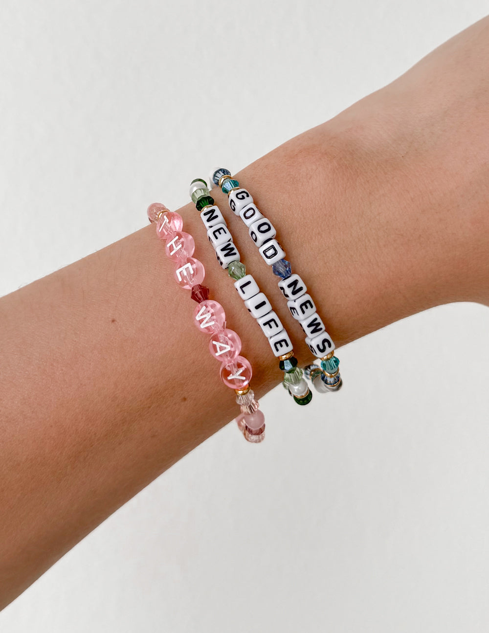 Stacked beaded letter bracelets on wrist with pink beads and black-and-white letter beads