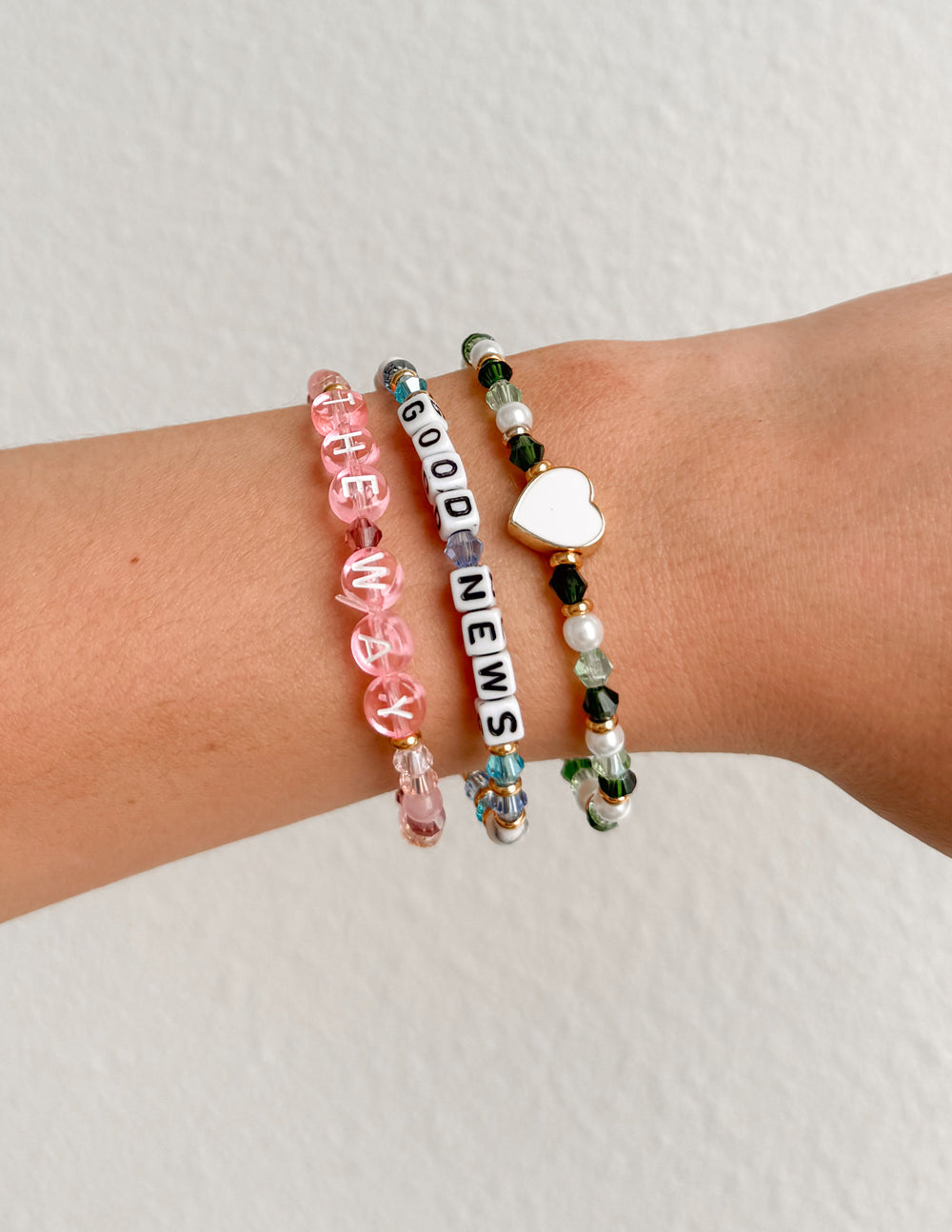 Beaded letter bracelets on wrist with heart charm and pink, black, and green beads