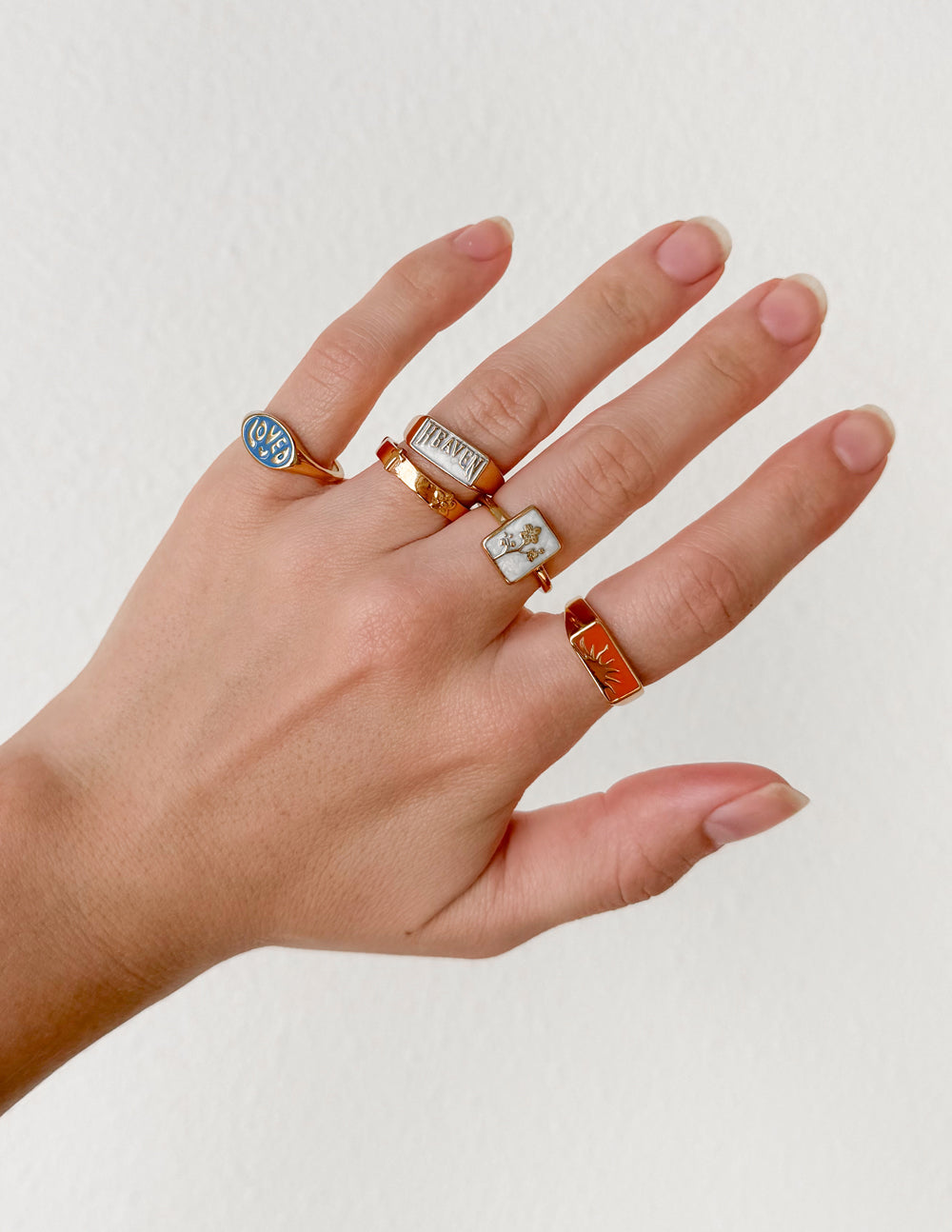 Stack of enamel rings: blue round, gold square, and orange accent on hand