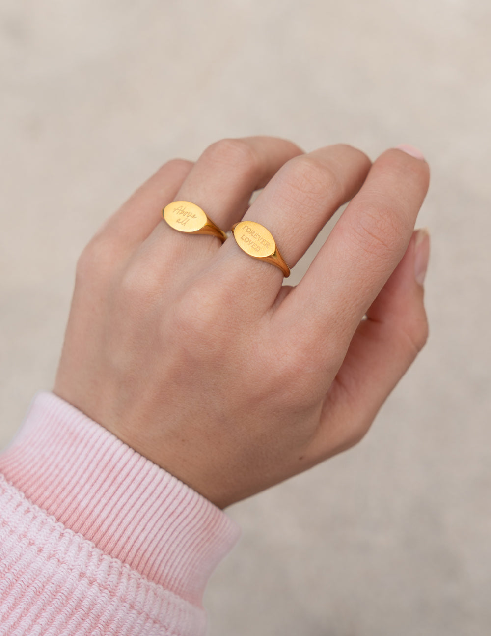 Pair of gold oval signet rings with engraved script on fingers