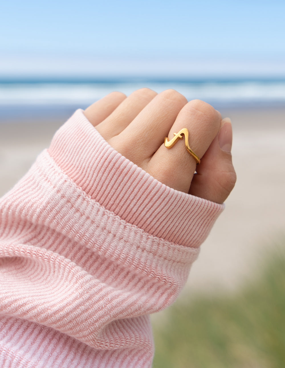 Gold wavy cross ring on finger, open curved band