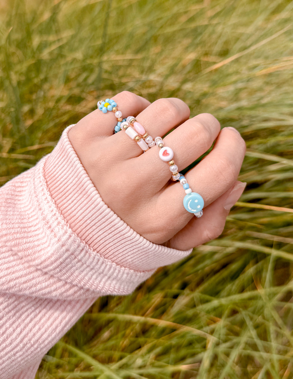 Stacked beaded rings on hand with light blue and white beads on gold-tone bands