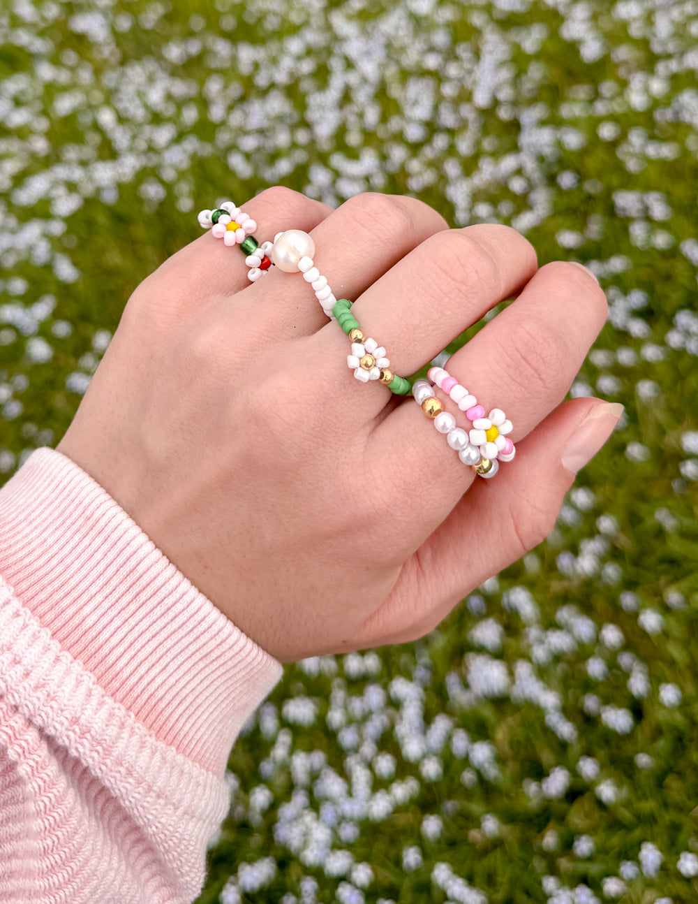 Beaded flower rings on hand with green and white bands and pearl bead details