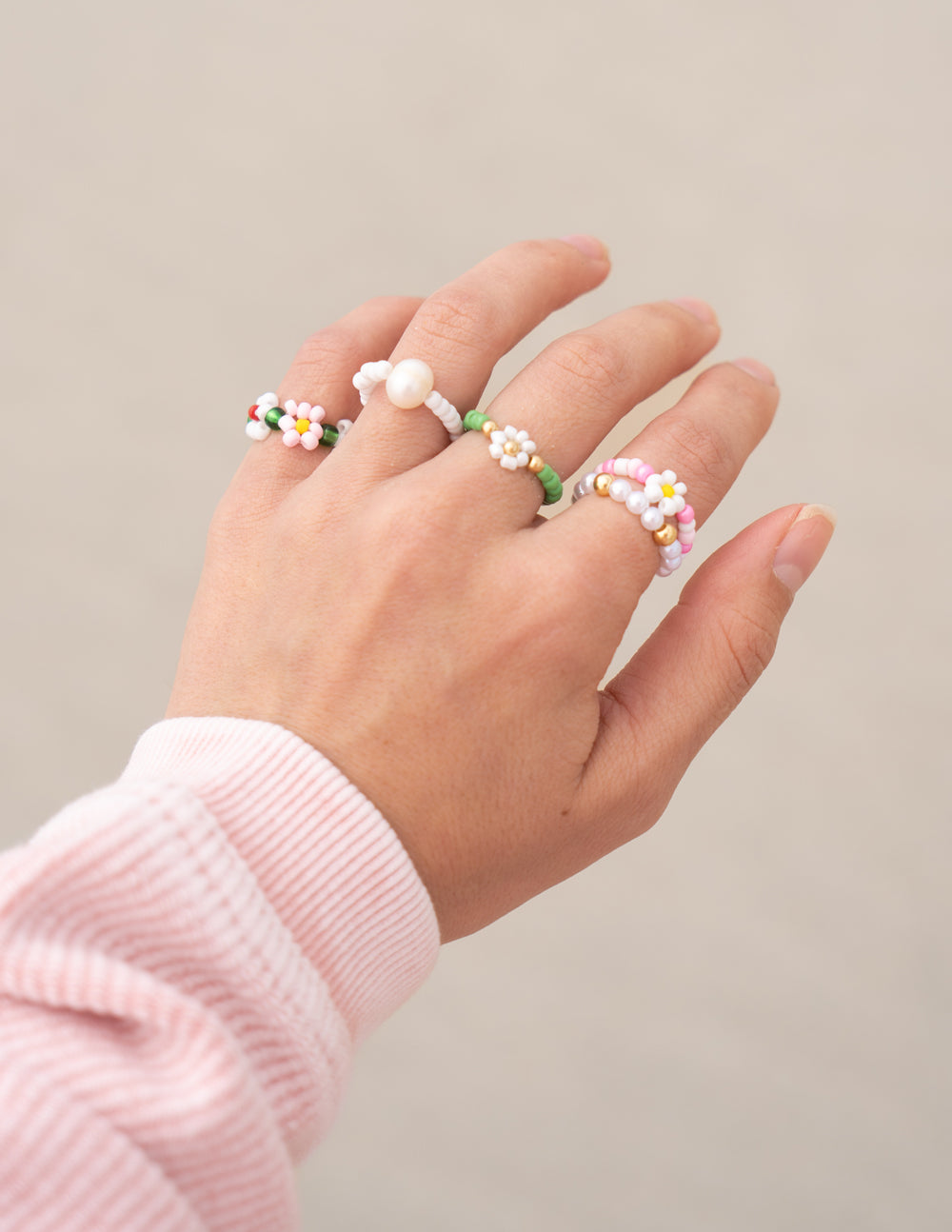 Beaded rings on hand: multicolor flower clusters, pearl beads, green and white bands