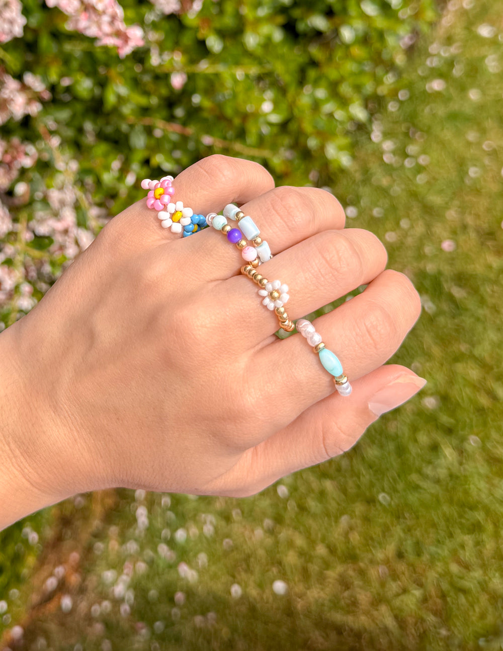 Pastel beaded rings close-up on hand with daisy-style and white bead details